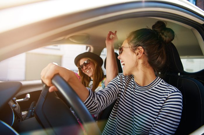 Two young women having fun driving along the street singing and laughing