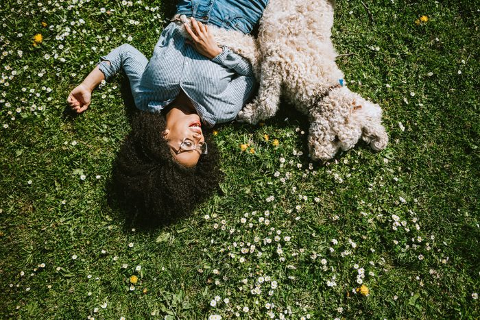 young woman lying on grass outside with her low maintenance white dog