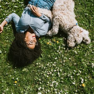 young woman lying on grass outside with her low maintenance white dog