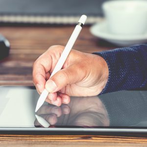 man signing on a tablet with a stylus pen at a wooden desk