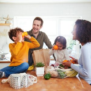 Family Returning Home From Shopping Trip Using Plastic Free Bags Unpacking Groceries In Kitchen