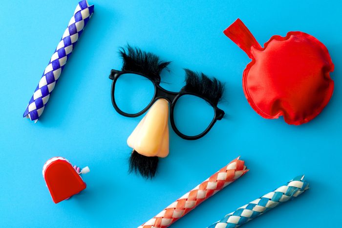 Comical prank, April fools practical joke and goofy disguise concept farting bag, chattering teeth, chinese finger trap and novelty glasses with fake nose and eyebrows isolated on blue background