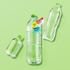 three various plastic water bottles on green background. center bottle has expiration stickers on it