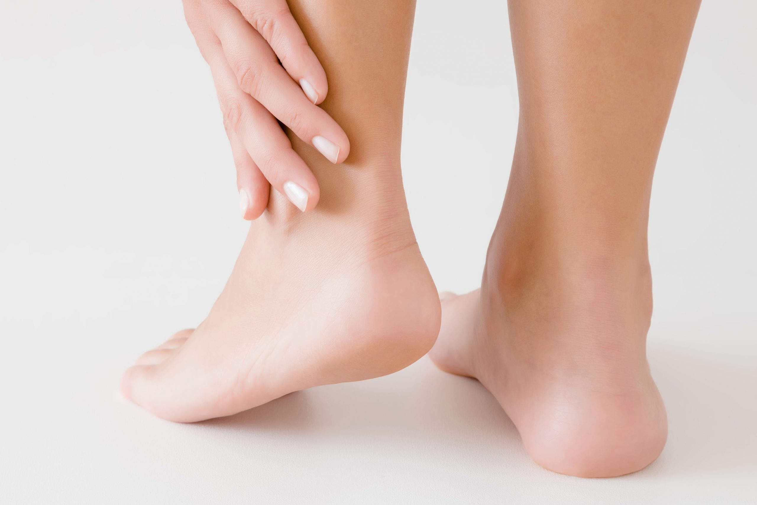 Young woman's hand touching perfect groomed legs on gray background. Tired feet. Care about clean, soft, smooth skin. Closeup. Back view.