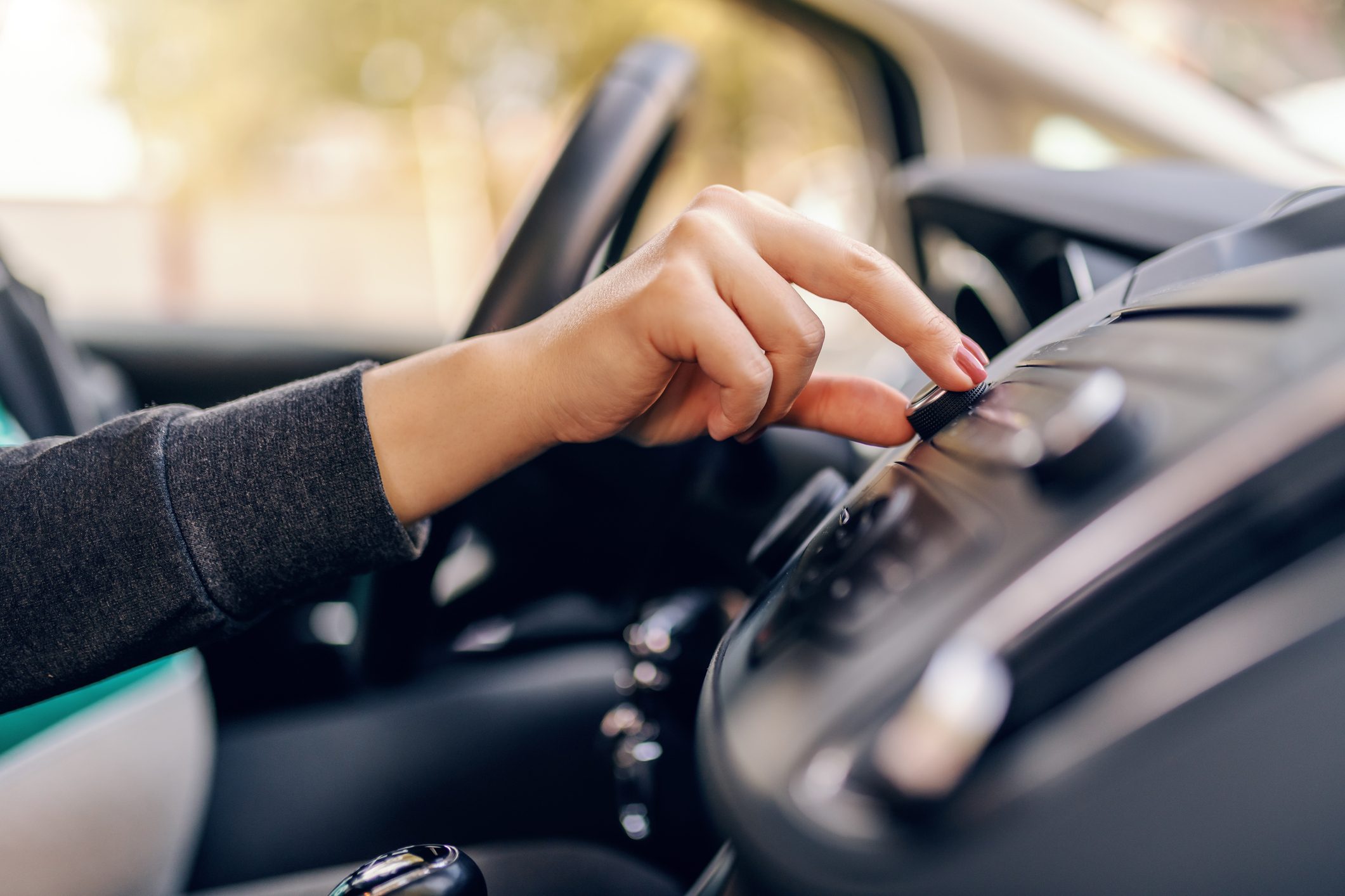 Close up of pregnant woman searching radio station while sitting in car. Other hand on steering wheel.