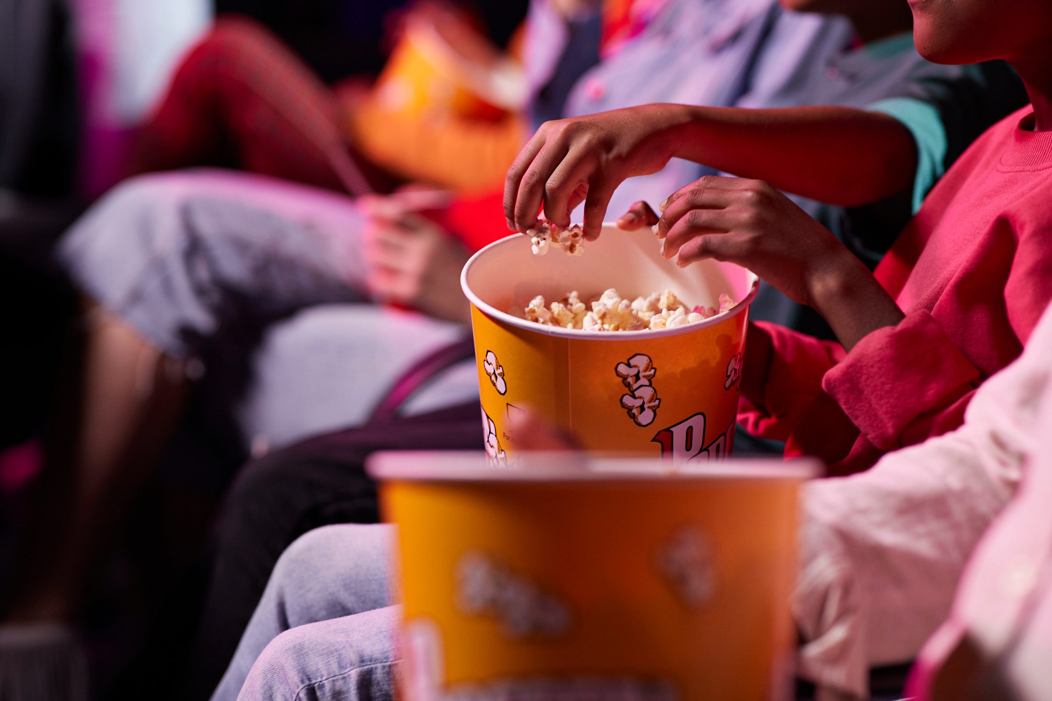 Midsection of friends sharing popcorn while sitting in theater