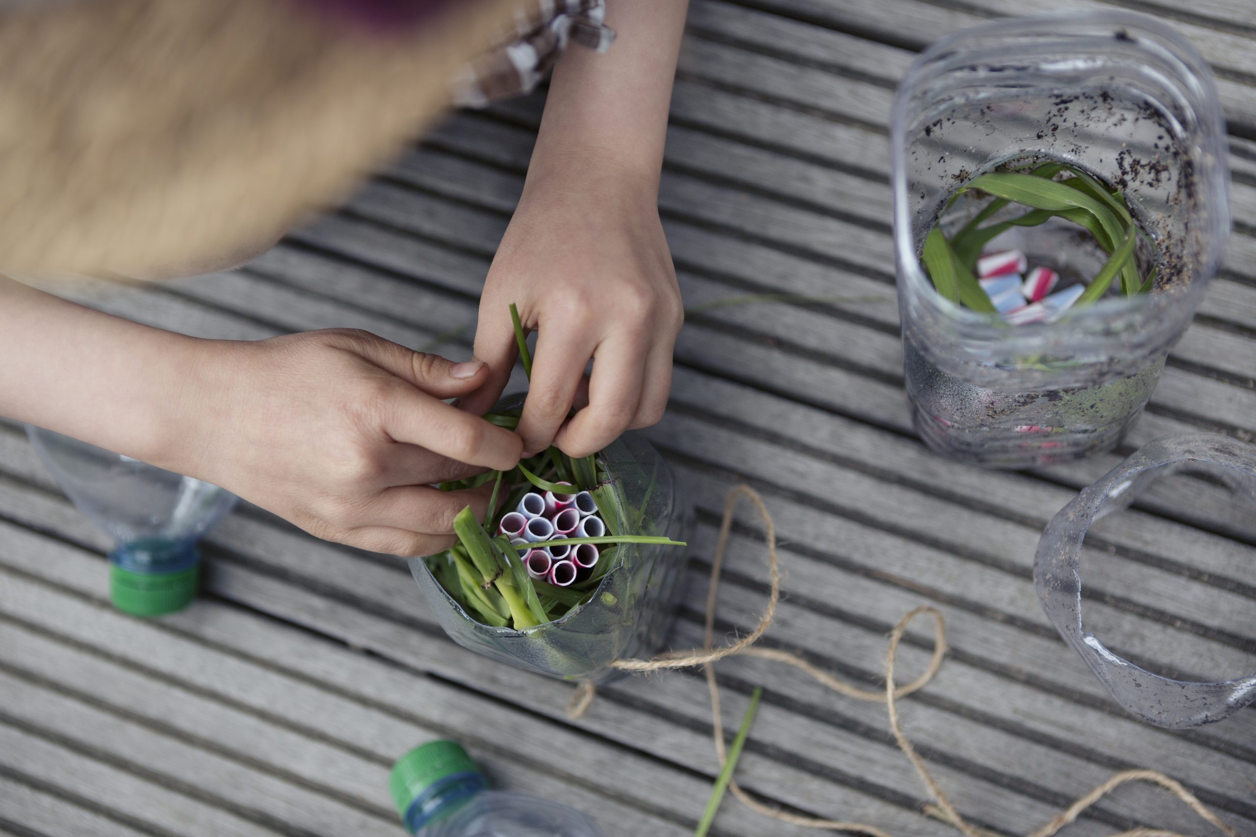 Child (6-7) using recycled plastic straws and bottles to repurpose into an insect house