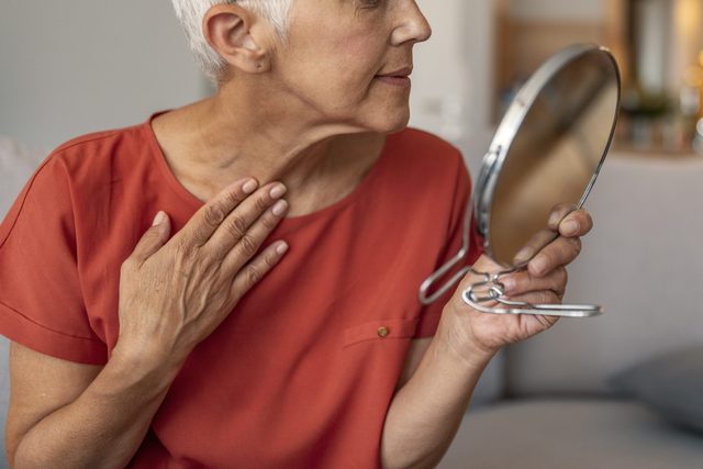 Mature woman with make-up mirror massaging her face and neck