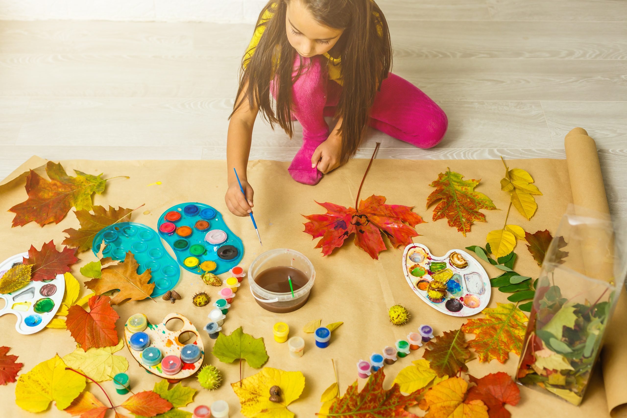 Little girl painting on autumn yellow leaves with gouache, kids arts, children creativity, autumn art.