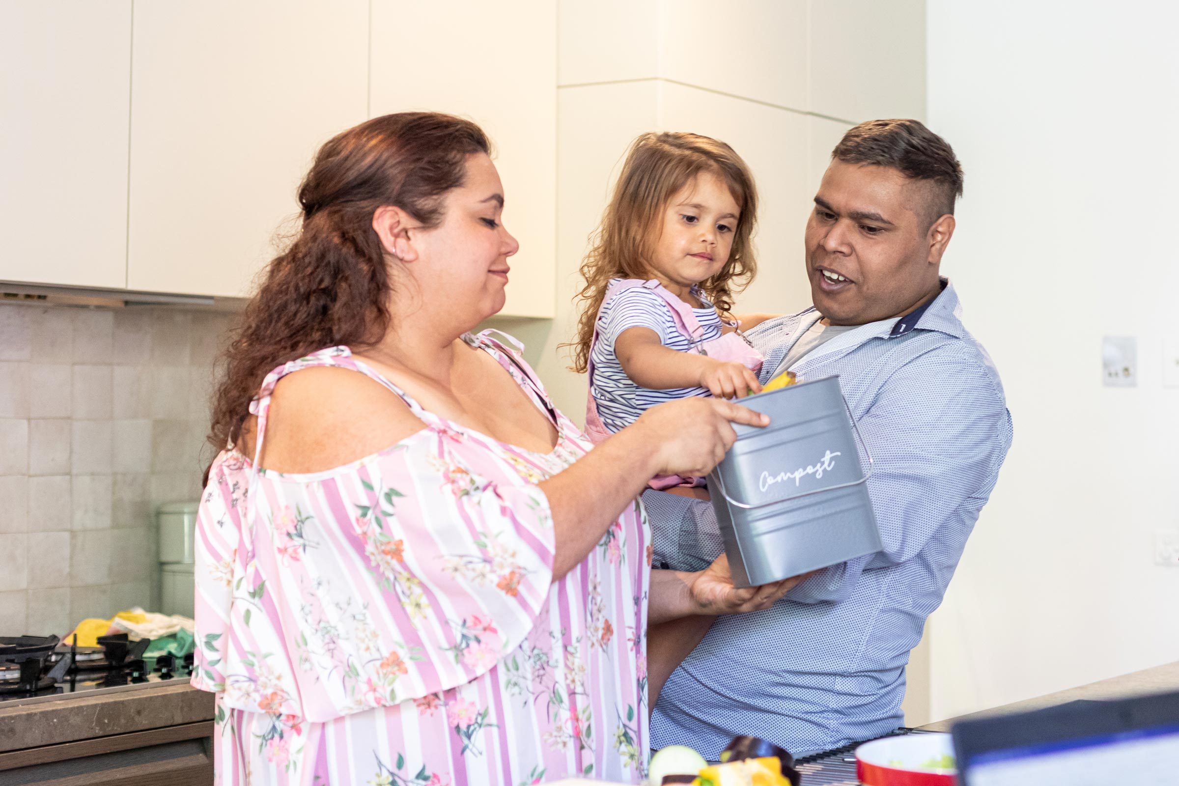 mother and father holding a little girl and a bin labeled Compost in the kitchen