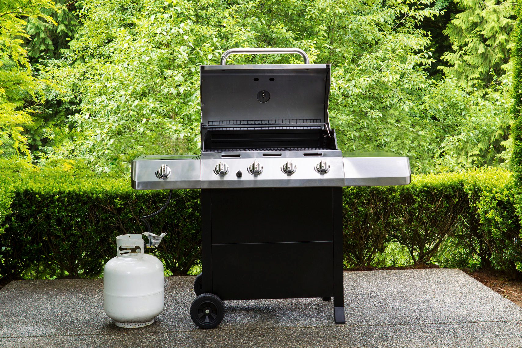 Large outdoor bbq cooker with lid in open position on home concrete patio