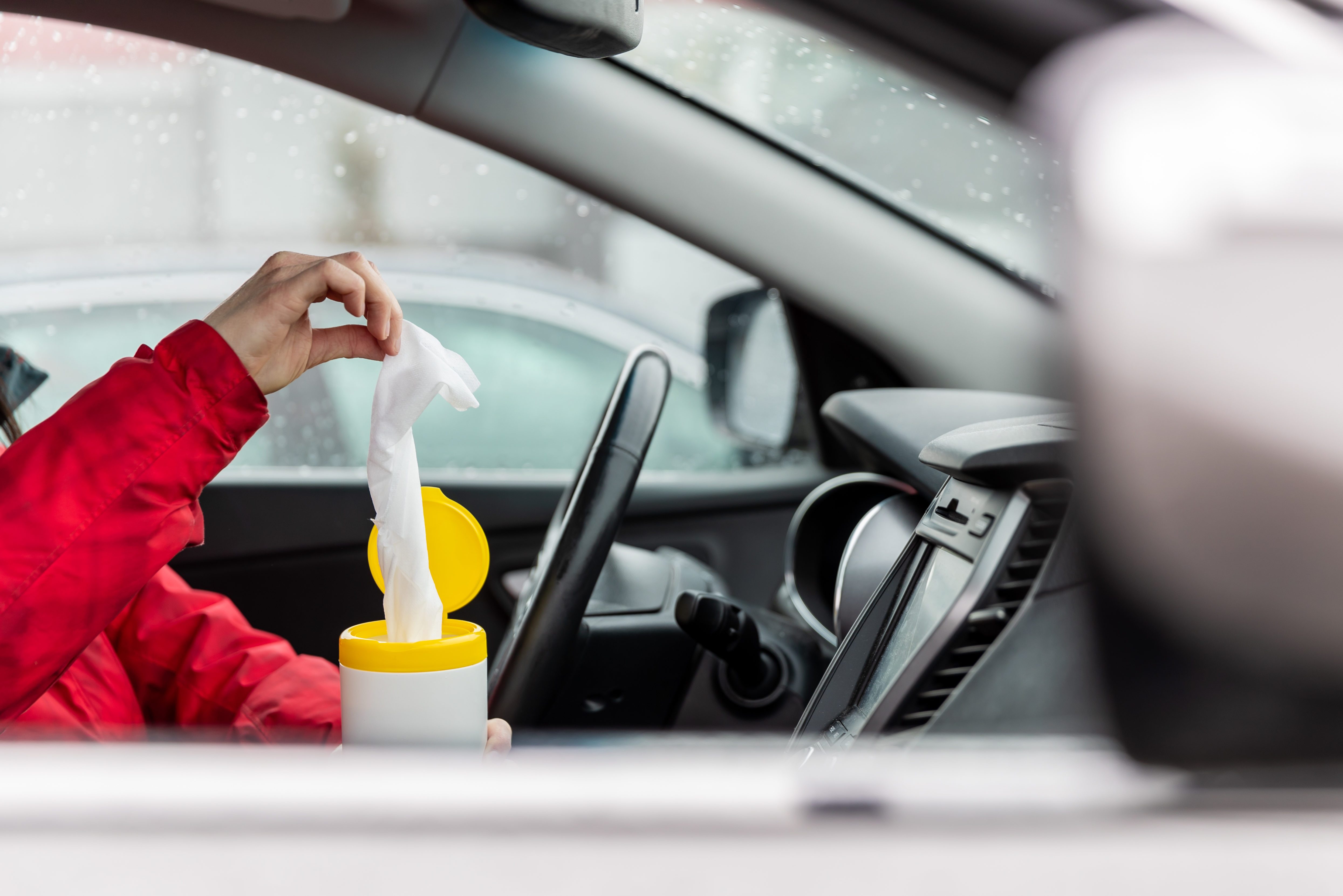 Woman using wet wipes to clean the steering wheel of a car