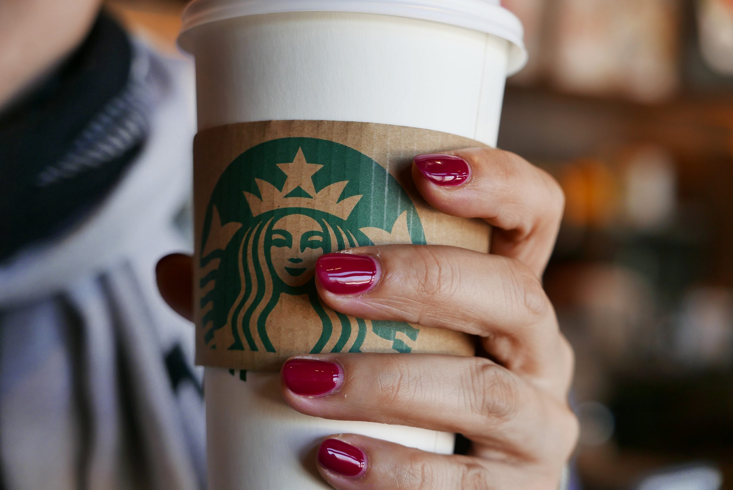 Hand holding a coffee cup in a Starbucks coffee shop. In...