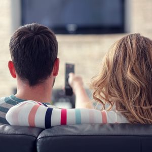 Happy young couple relaxing and watching TV at home.