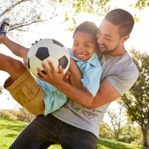 Father And Son Playing Soccer In Park Together