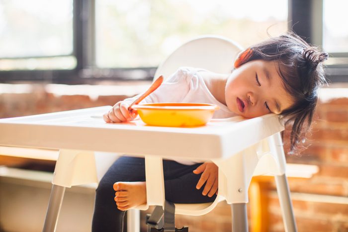 One year old baby girl asleep in highchair at breakfast