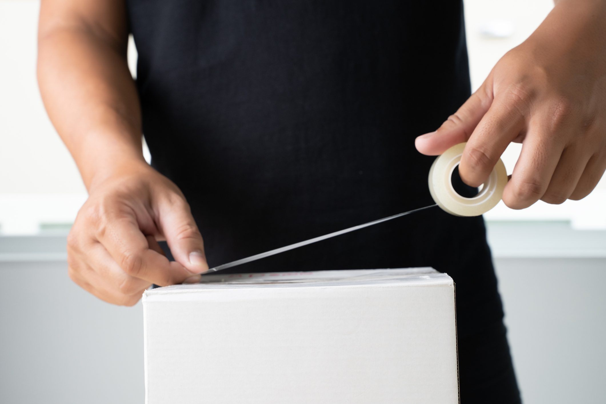 Midsection Of Man Applying Adhesive Tape On White Box At Home