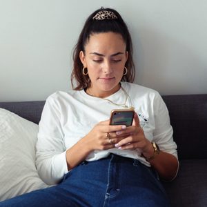 Young Woman Using Mobile Phone While Sitting On Sofa At Home