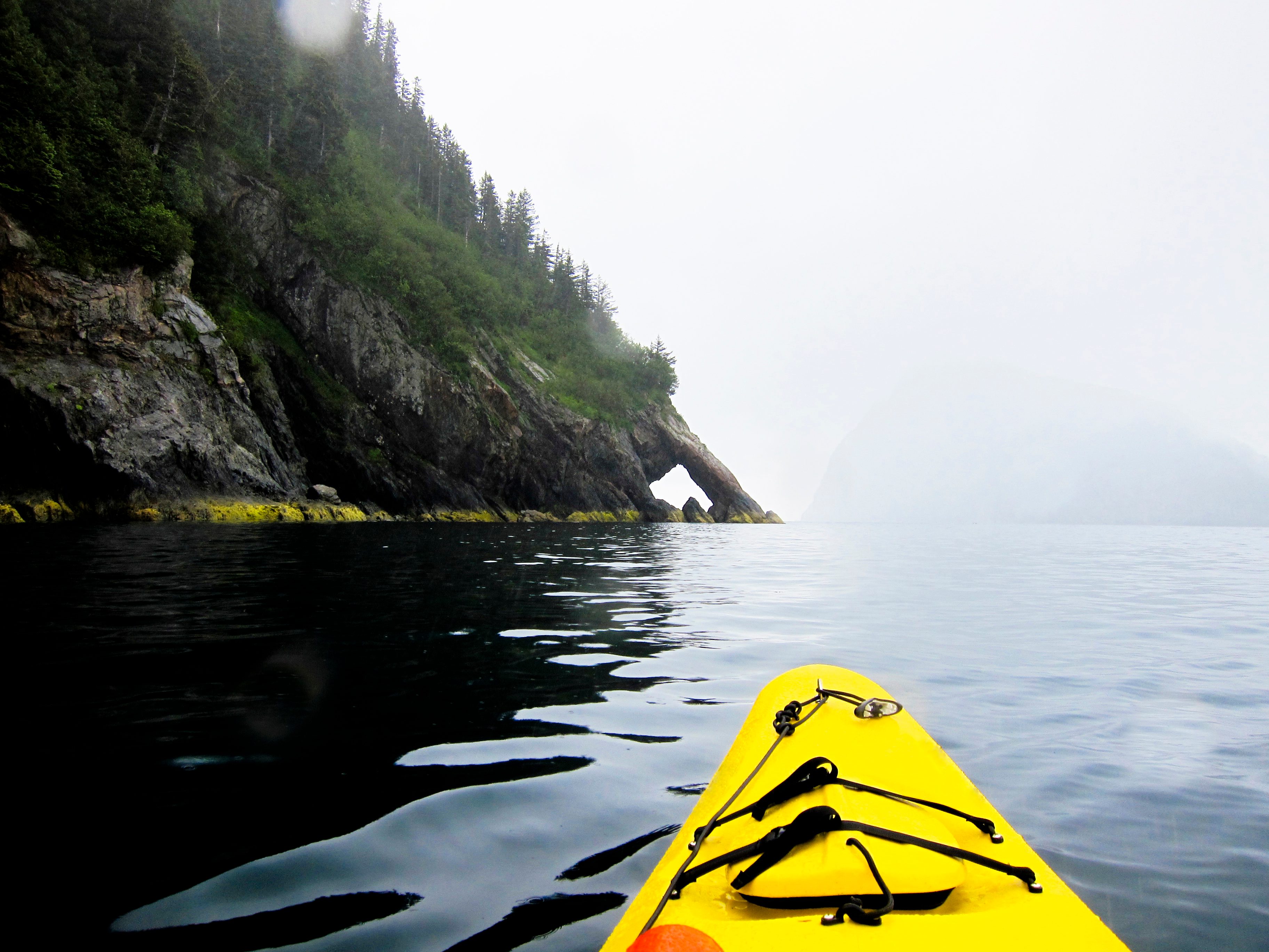 A pair of sea kayakers paddles during a grey Alaska summer day on the Pacific Ocean along Fox Island, Alaska.