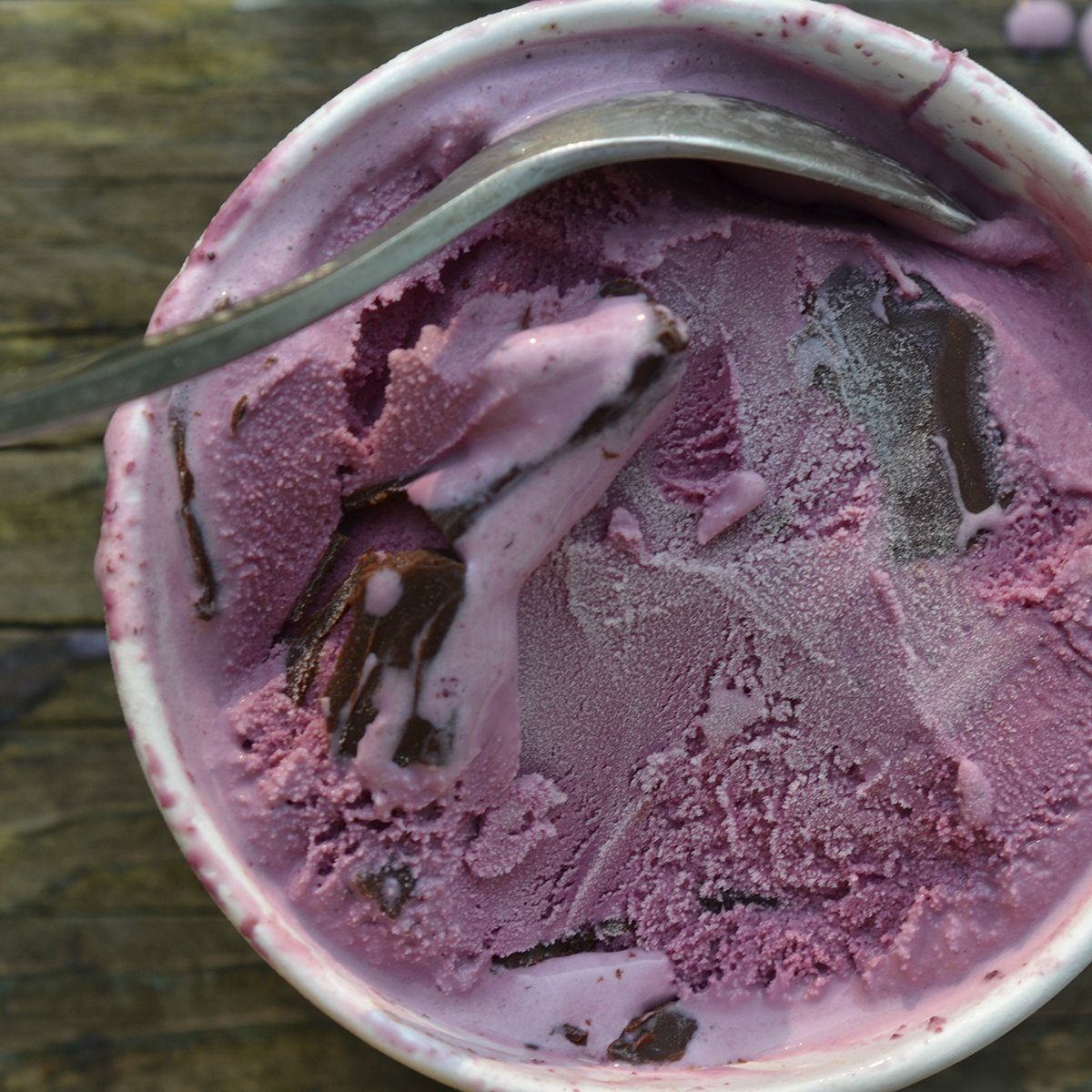 overhead view of a carton of black raspberry ice cream with chocolate chunks and spoon on wooden tabletop