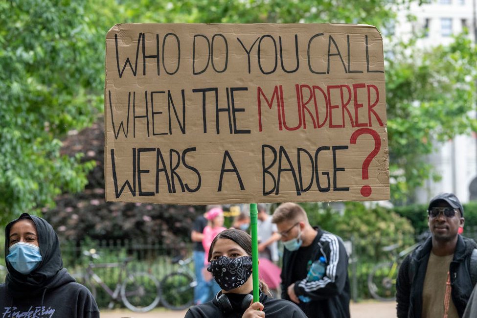 A protester holds a placard with Who do you call when the...