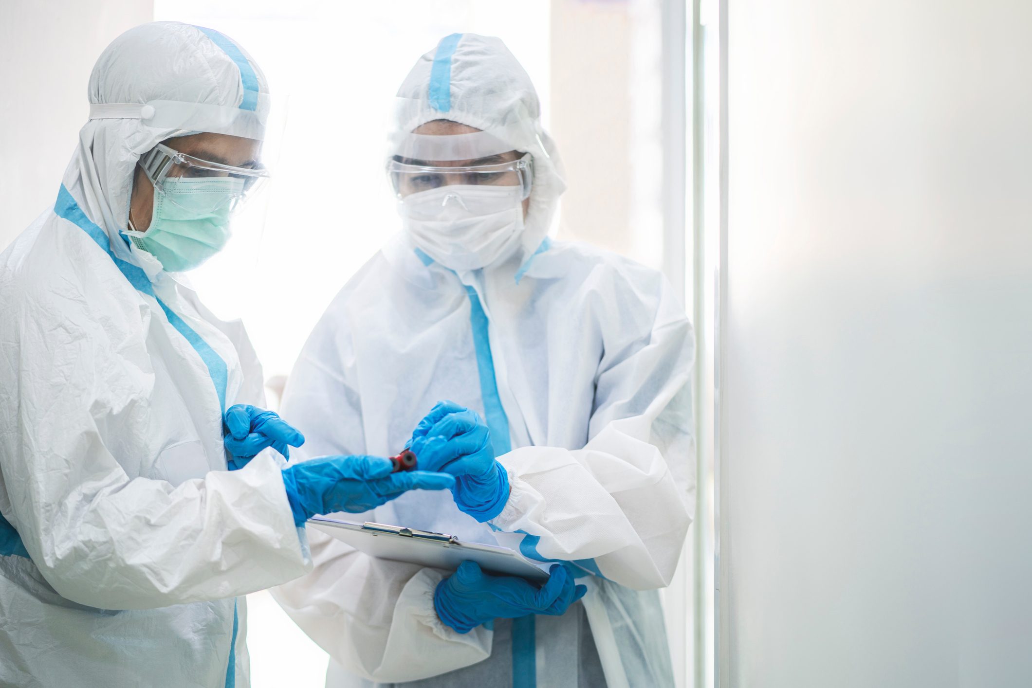 Asian doctor in PPE medical suit holding coronavirus or covid-19 blood testing tube in quarantine room