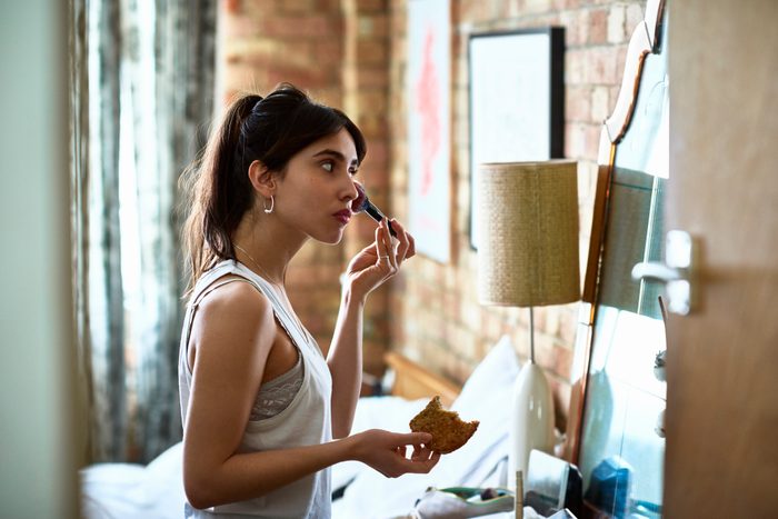 Young woman applying blusher with make up and holding toast