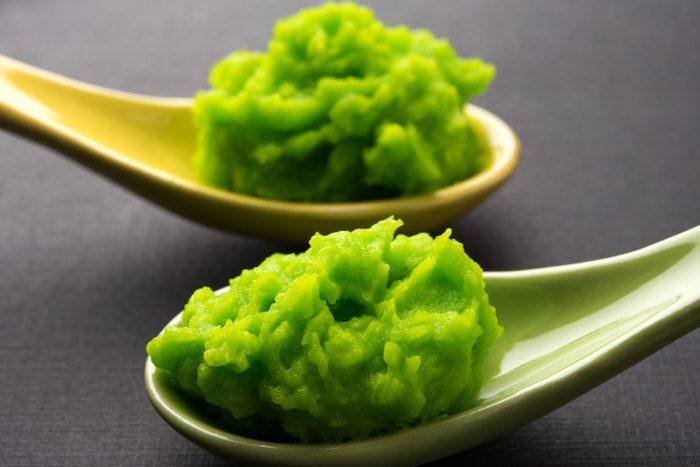 Green wasabi sauce or paste in bowl, with chopsticks or spoon over plain colourful background. selective focus
