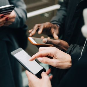 Midsection of colleagues using mobile phones while standing on road in city