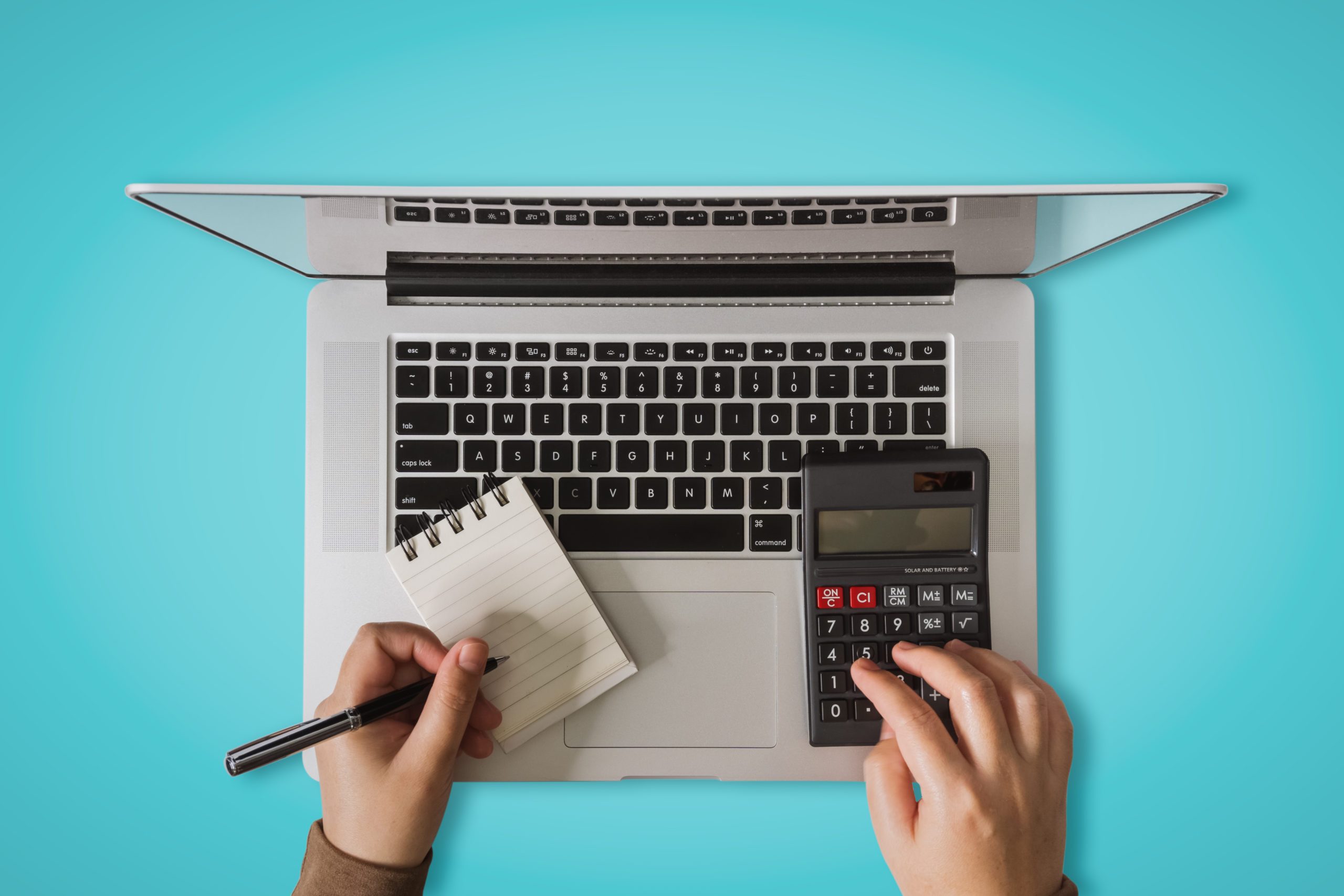 Overhead View of Hand Writing on Notebook and Using Calculator and Laptop