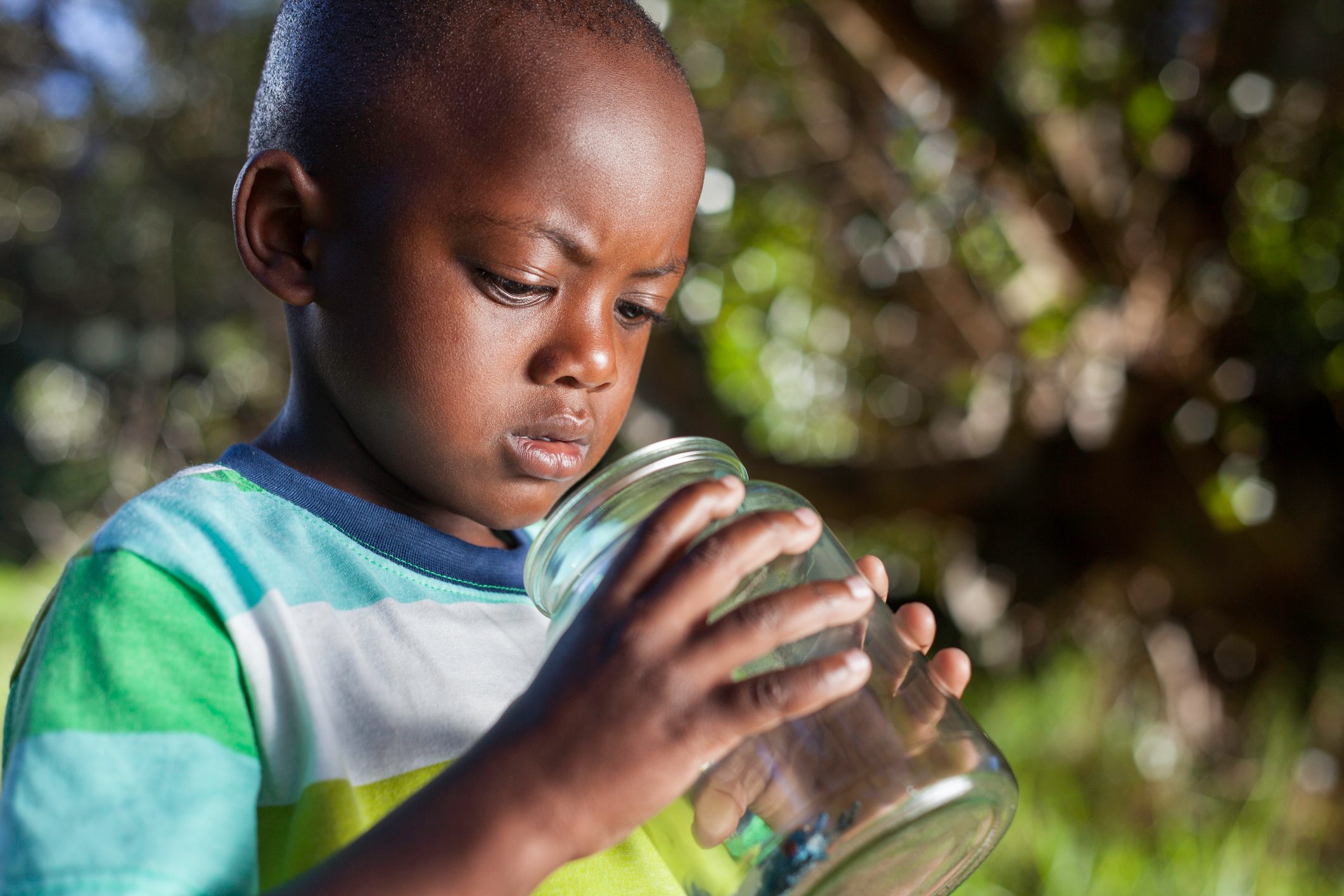 African child inspects bug in glass jar in his garden
