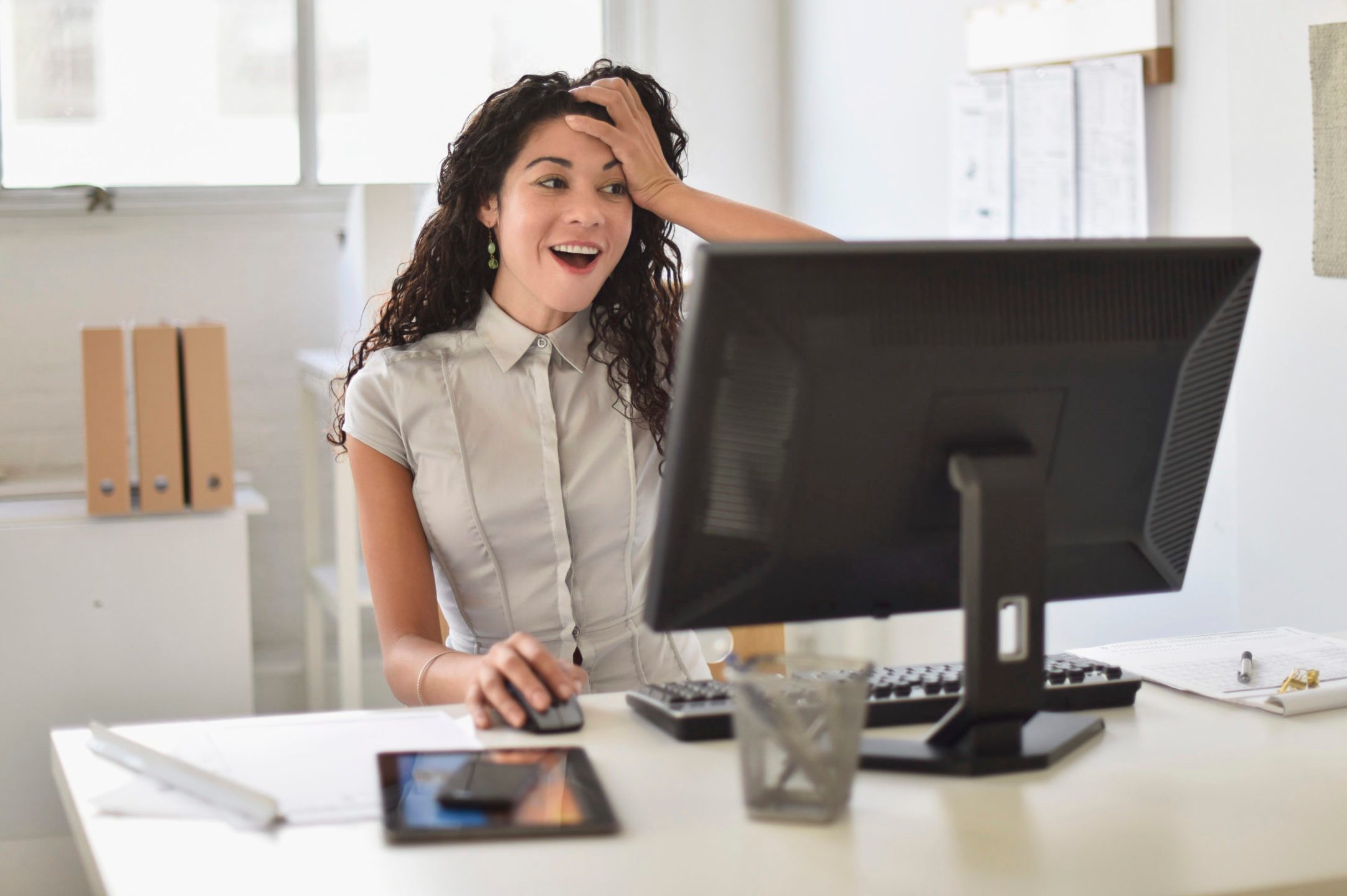 Mixed race businesswoman gasping at computer at desk in office