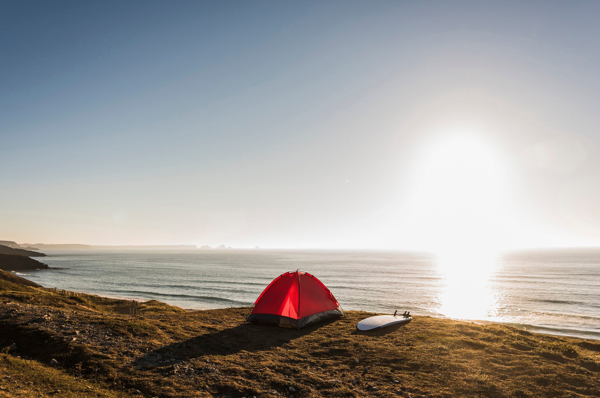 Red tent and surfboard at seaside in the evening twilight