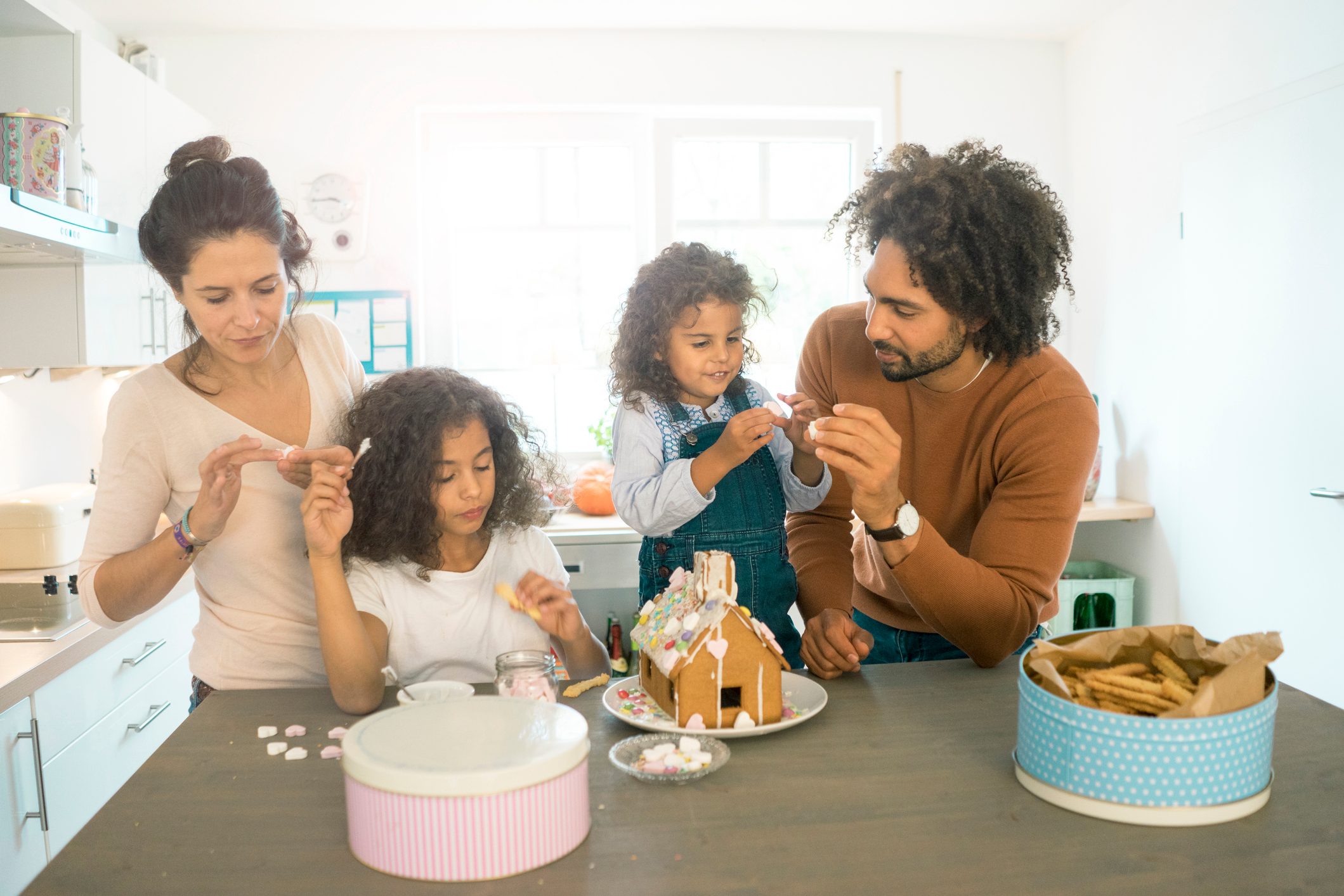 Family pasting gingerbread house in kitchen for Christmas with sweets