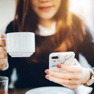 Close up of young woman having coffee and reading news on mobile phone in the early morning before work