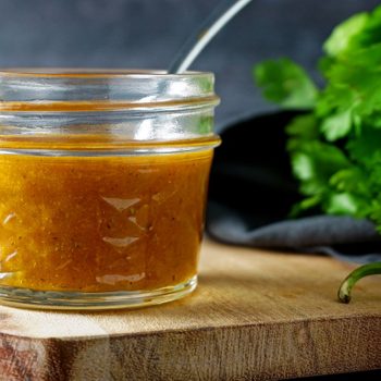 copycat chipotle honey vinaigrette in a faceted glass mason jar with a spoon on a wood and marble cheese board