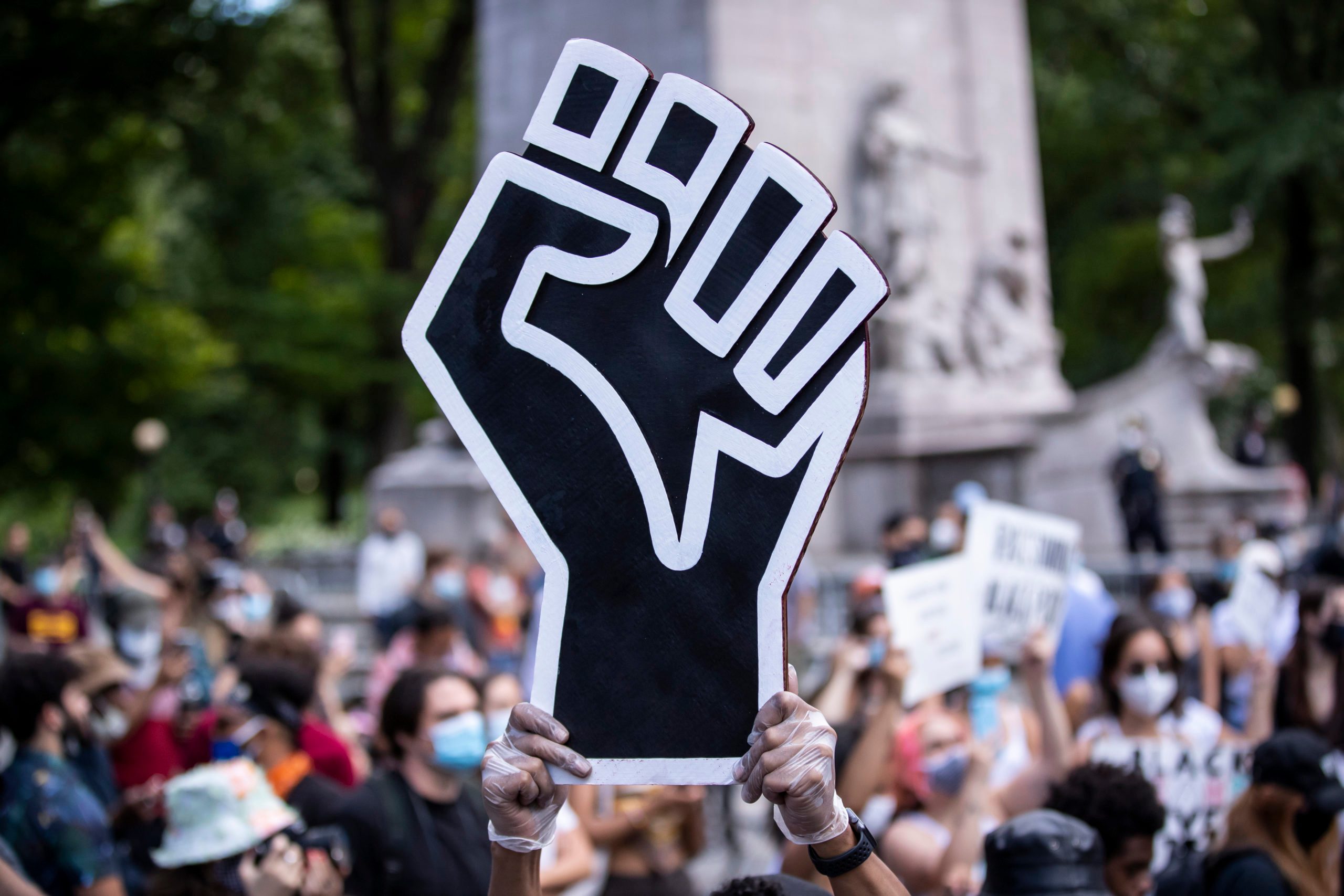 A protestor holds up a large black power fist in the middle of a crowd gathered at Columbus Circle in New York City for a George Floyd Black Lives Matter Protest