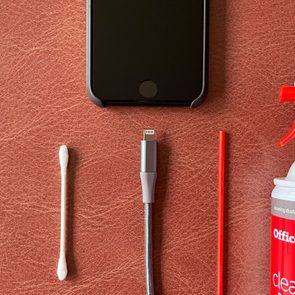 close up of iphone charging port with lightning cord and cleaning supplies; q-tip cotton swab and can of compressed air