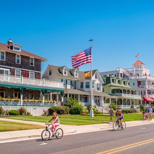 People bike and walk in front of traditional villas in Cape May, New Jersey, USA, on a sunny summer day.