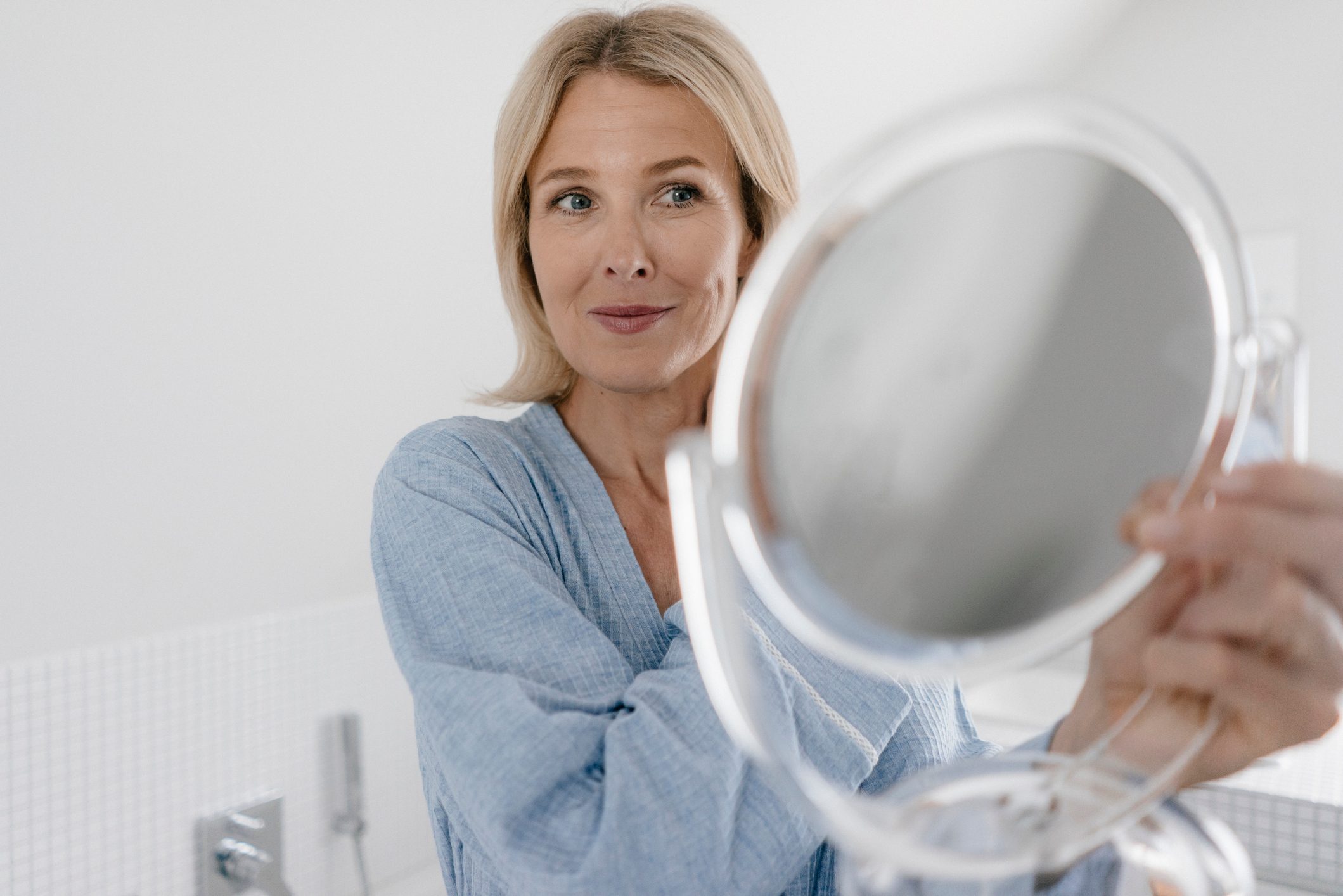 Mature woman looking in beauty mirror in bathroom