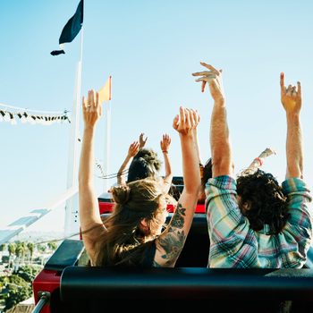 Rear view of couple with arms raised about to begin descent on roller coaster in amusement park