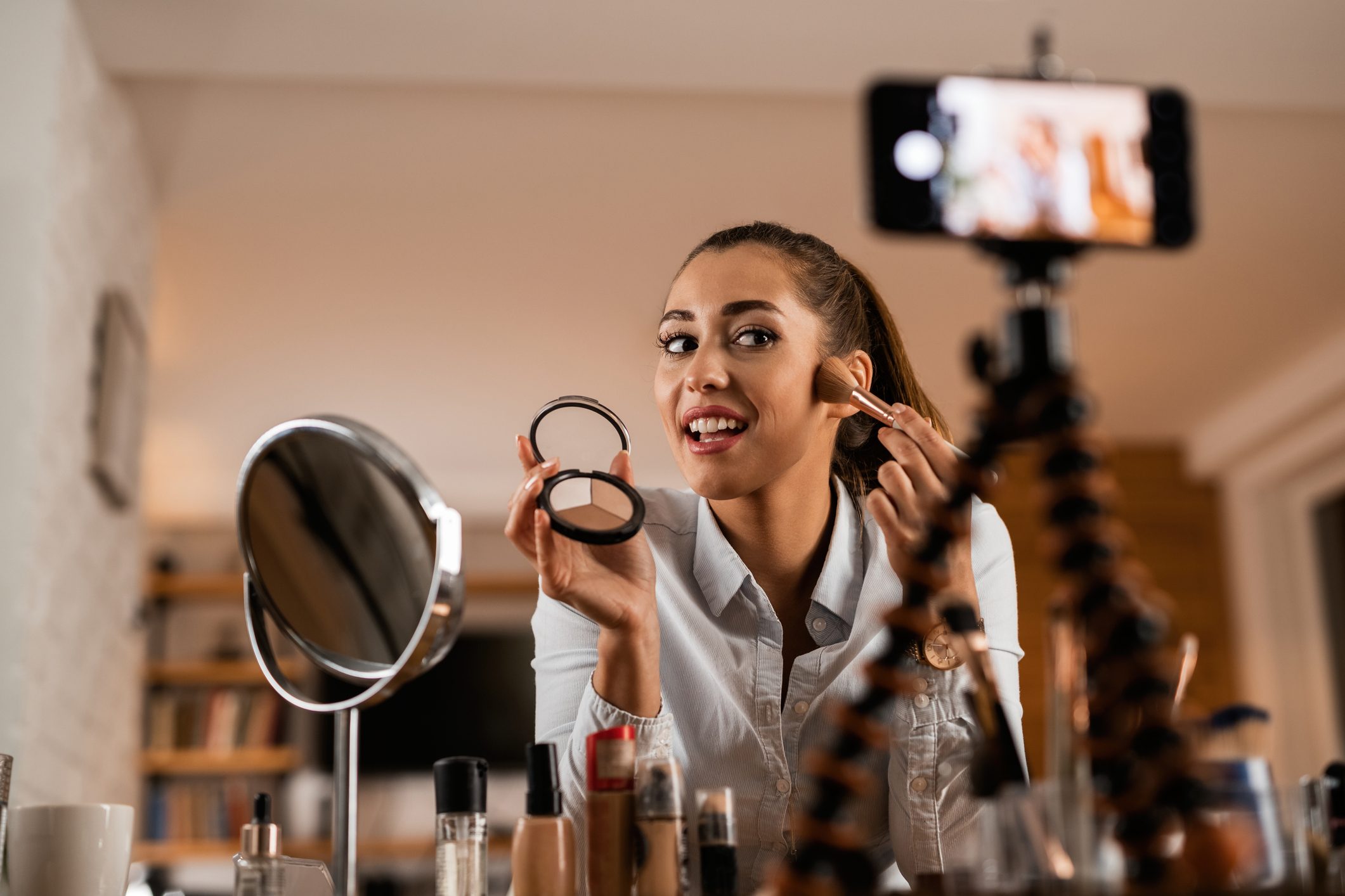 Beautiful woman recording face contouring and highlighting vlog at home.