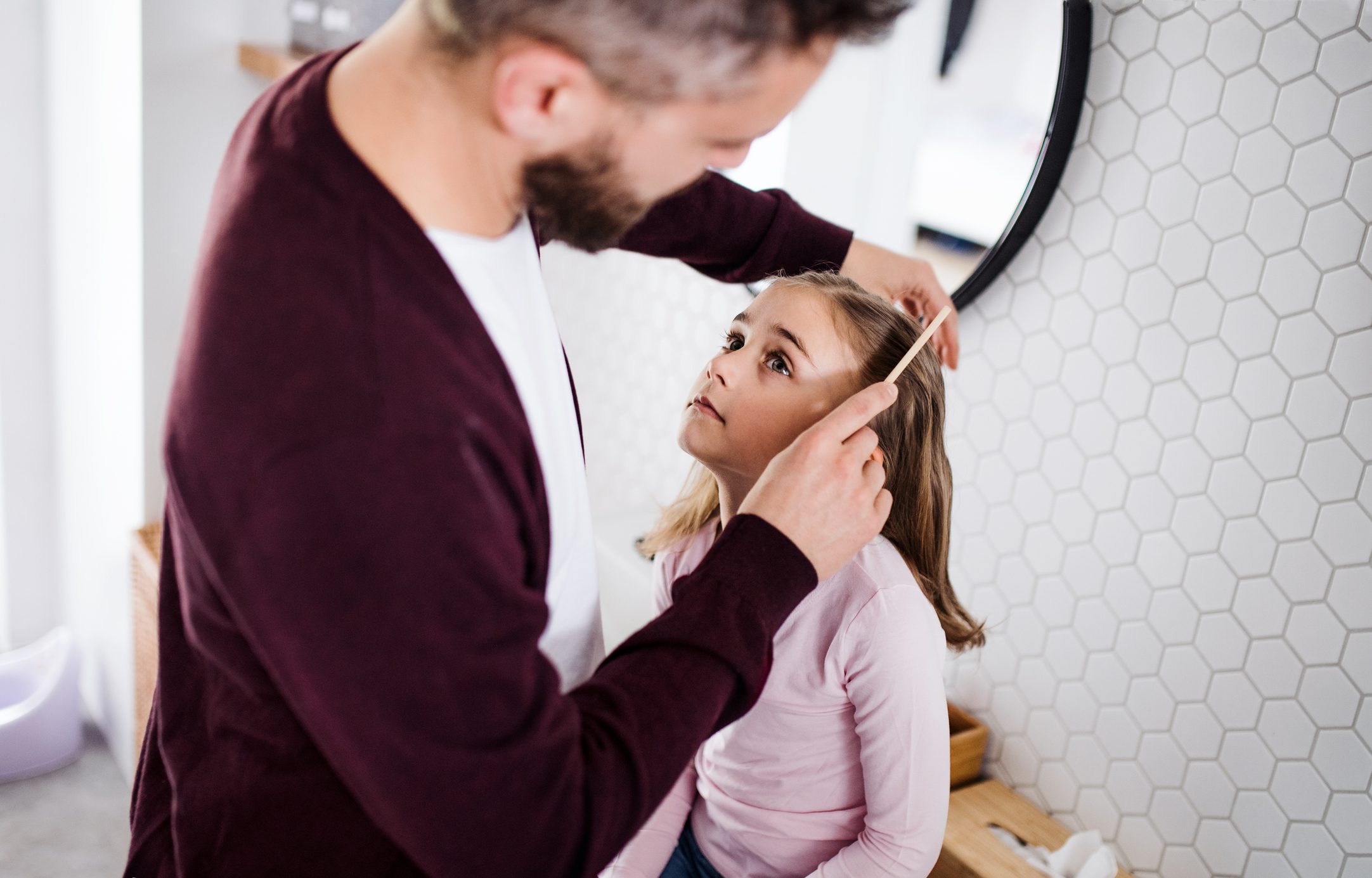 Mature father and his small daughter in bathroom indoors at home, combing hair.