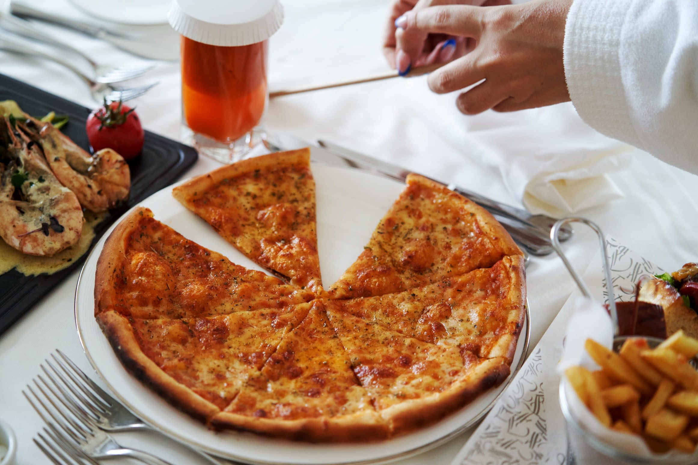 Pizza slices, Shrimp in sauce and french fries on a white table close-up