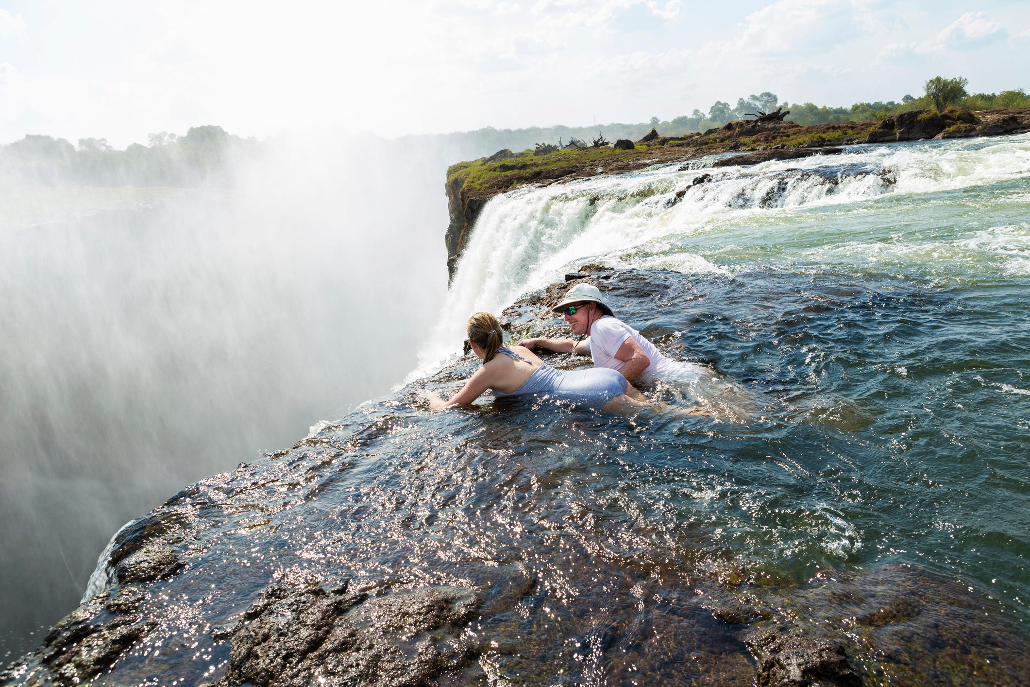 Man and a girl, father and daughter in the water of the Devil's Pool on the edge of Victoria Falls, mist rising from the falling water.