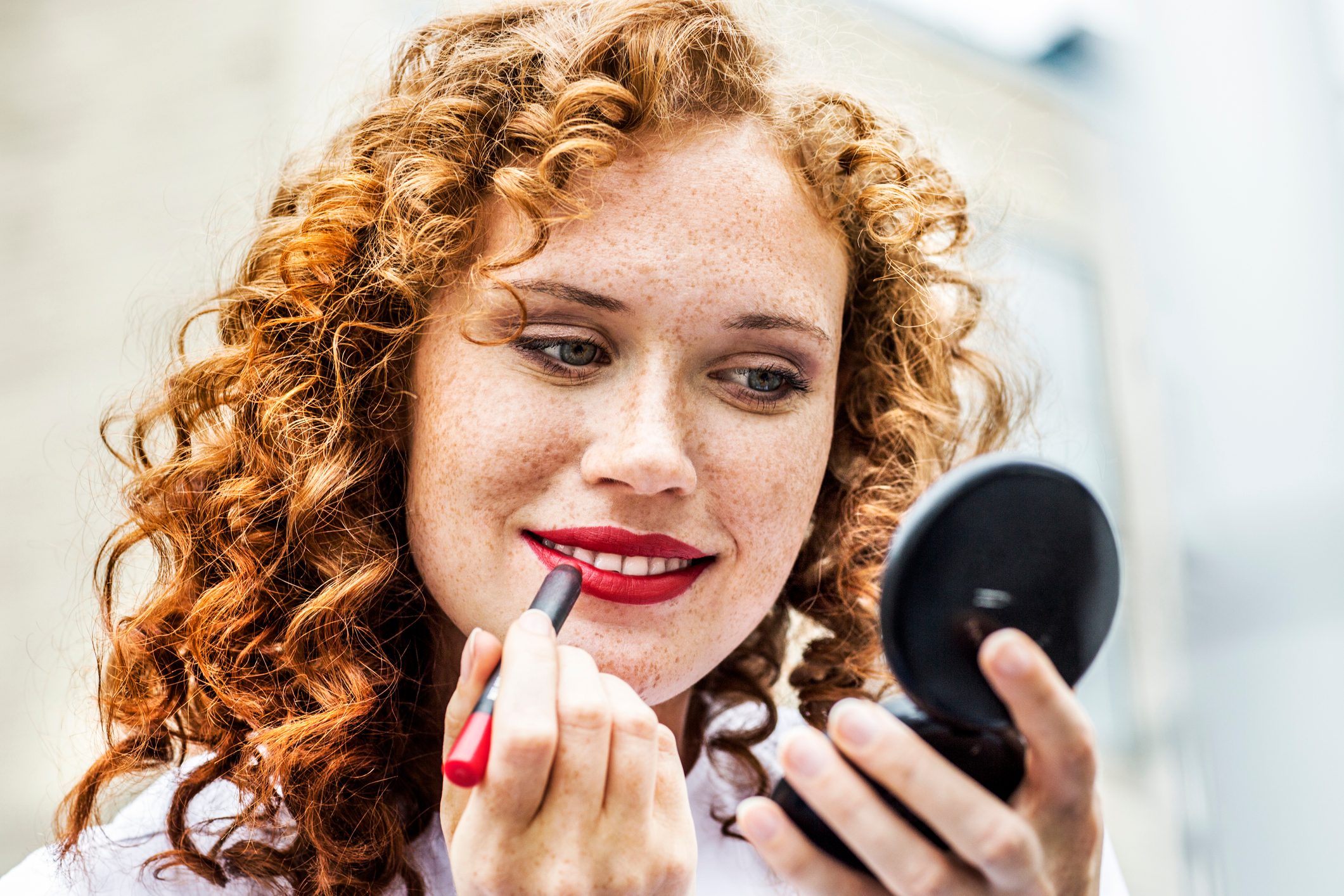 Portrait of freckled young woman applying lipstick