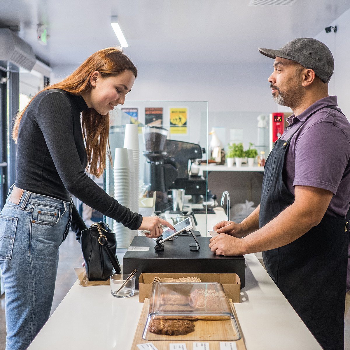 Teenage girl paying for her coffee at the register. She signs the bill with her finger on the cash register tablet.