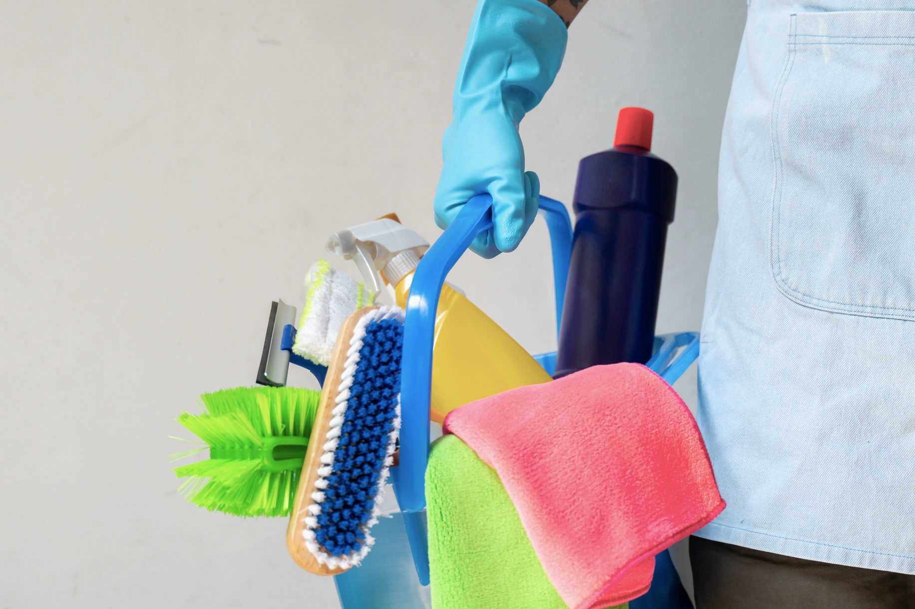 Man holding mop and plastic bucket with brushes, gloves and detergents in the kitchen