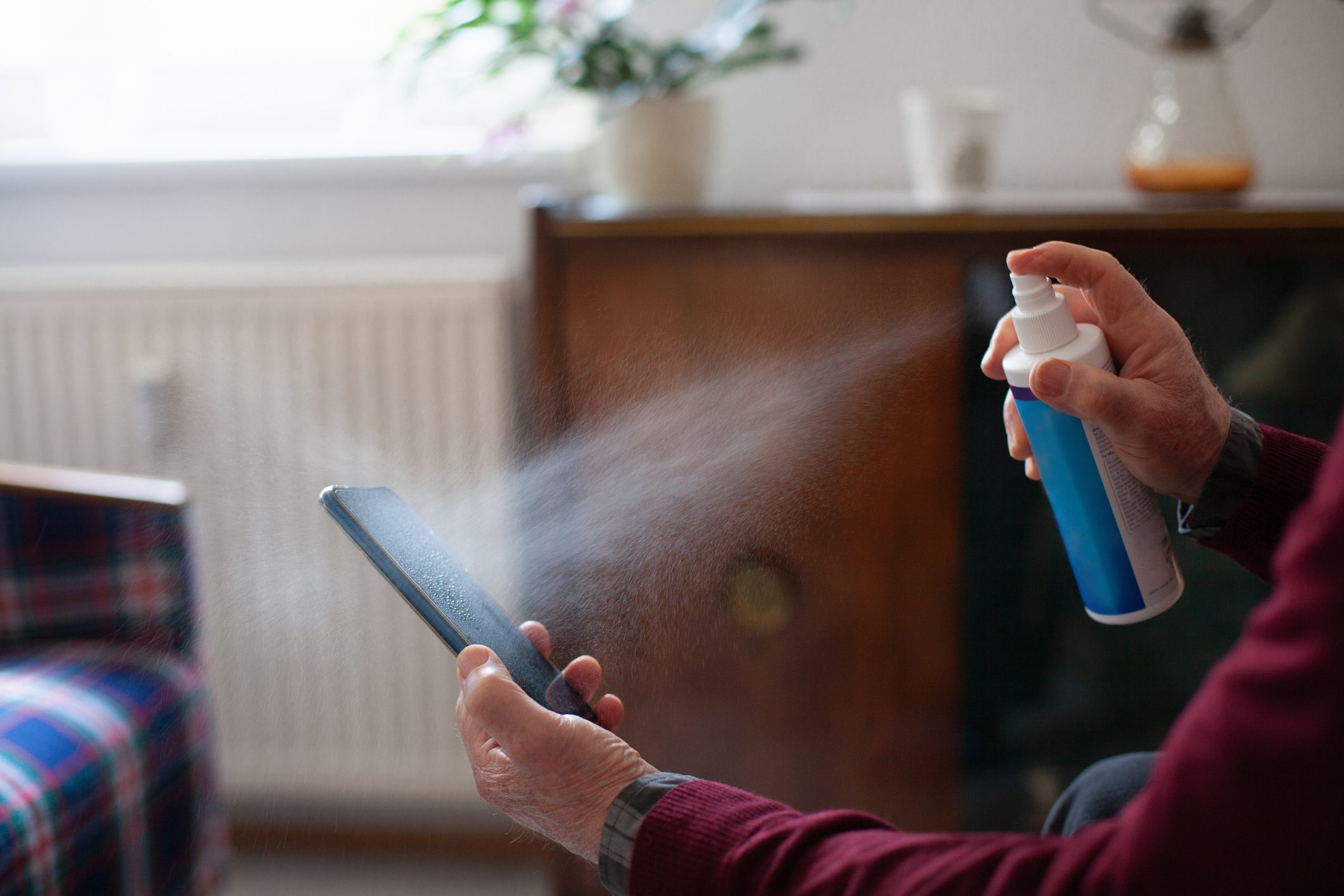 Senior man obsessively cleaning his mobile phone with disinfectant spray, close-up of hands