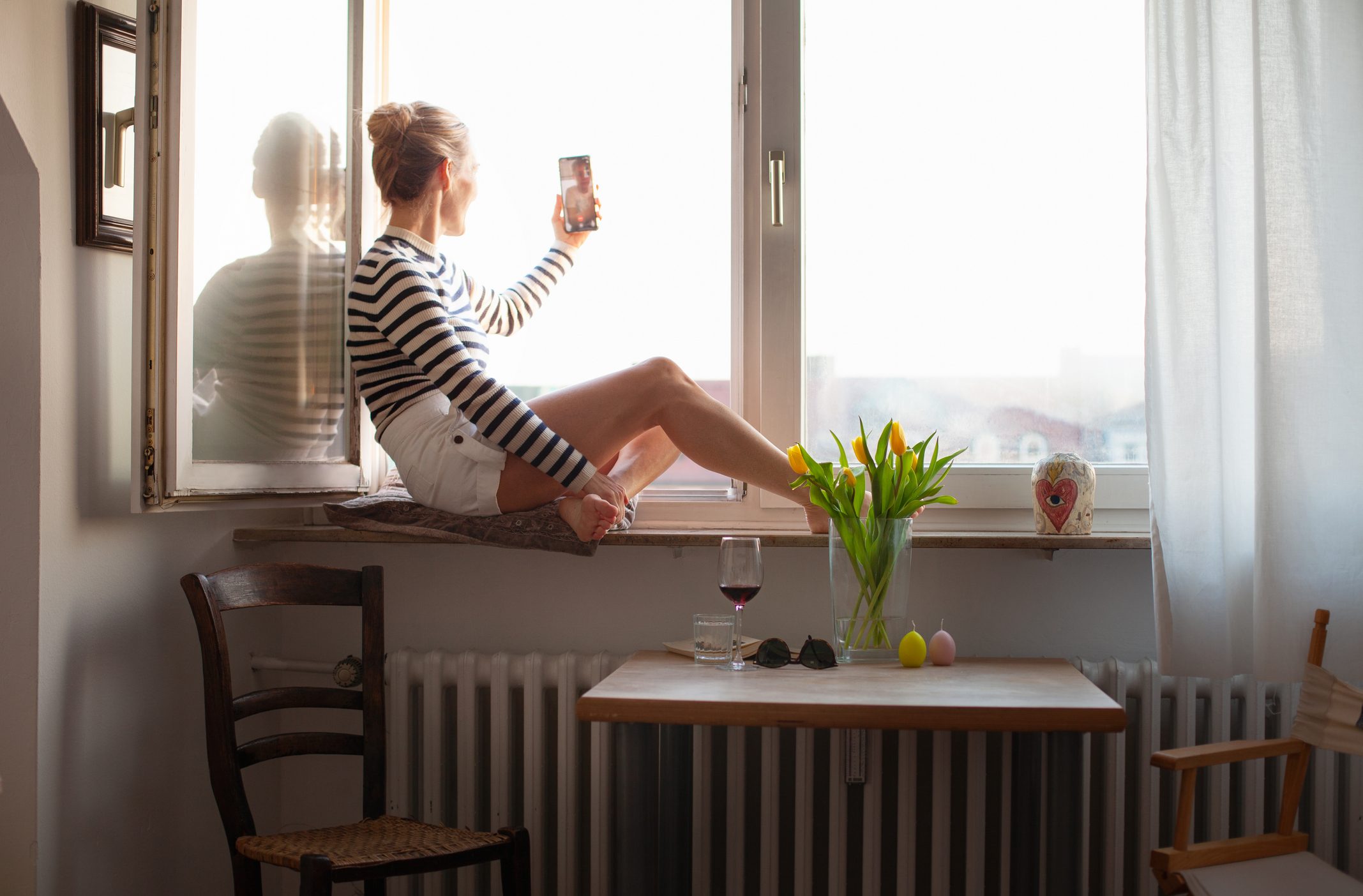 Woman sitting on a windowsill, video chatting with family member